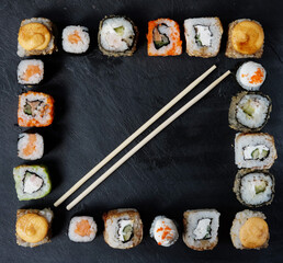 A variety of sushi with wooden desk on black slate background. Asian food frame.
