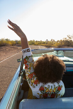 Black woman with arm raised driving vintage Automobile on Desert Roadtrip 