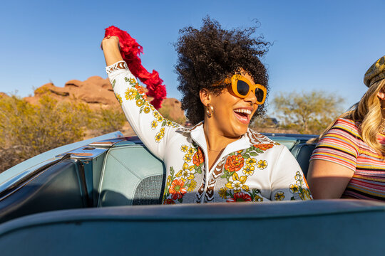 Black girl holding Red Feather boa in back seat of convertible car  