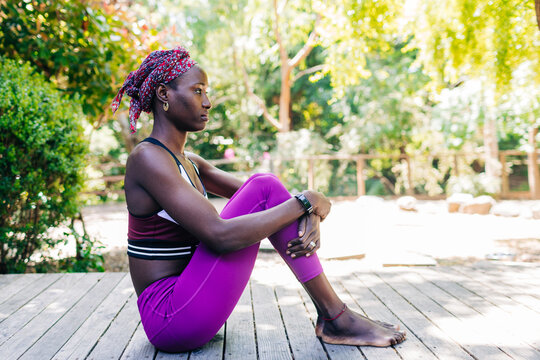 Serious young black lady sitting on wooden tribune after training in park