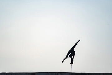 Silhouette of flexible girl dong handstand in split on sky background. Concept of willpower, motivation and passion