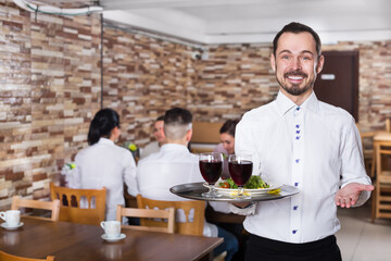 Fototapeta na wymiar Cheerful male waiter serving a rural restaurant guests at table