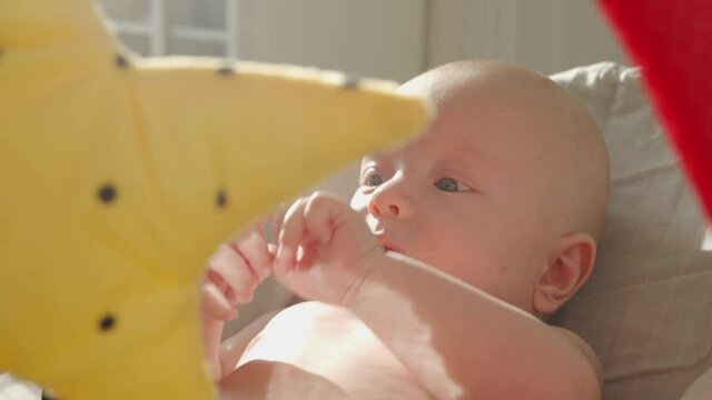 Baby face in sunlight, cute three month old baby boy rocking himself while sitting in rocking chair in front of toy mirror. High quality 4k footage