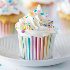 Close up of a frosted confetti sprinkle cupcake in a pastel striped muffin cup.