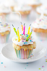 Close up of a frosted confetti sprinkle cupcake with many candles that have just been blown out. 