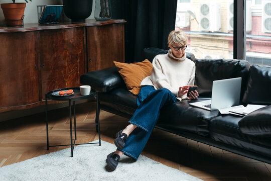 Middle-Aged Woman Using Electronic Devices Sitting On Sofa.