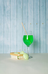 Green drink in a glass and green sweets on a wooden turquoise background, copy space