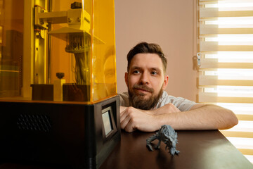 Man sitting by the table and looking 3d printing process 