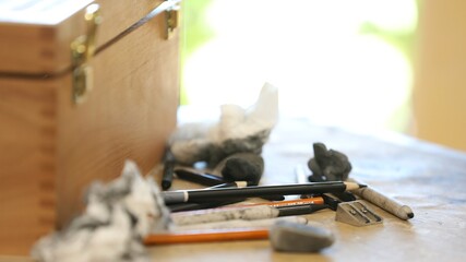 Close up detail of a variety of drawing media an artist or drawer would use creatively. Charcoal, pencils, sharpener and other artistic products on a table being used.