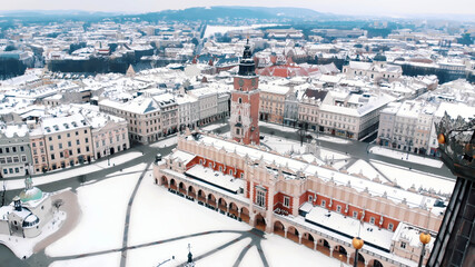 Drone view of Krakow's Town Hall Tower in the Main Market Square surrounded by historic townhouses and churches. Streets covered with snow in the winter season. City with ancient architecture. 