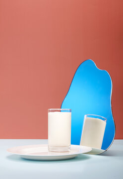 A glass cup and a mirror filled with milk, on a specially designed table top spliced by color blocks, close-up