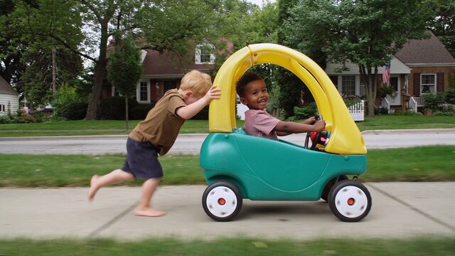 Caucasian boy pushing an African American boy in a toy car