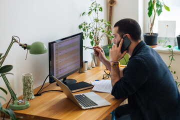 Handsome young adult man talking on the phone at home office. 