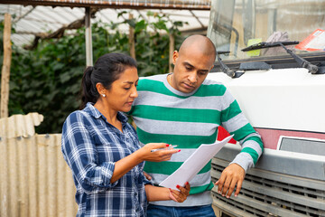 Two hispanic greenhouse workers signing documents and talking near car outdoors