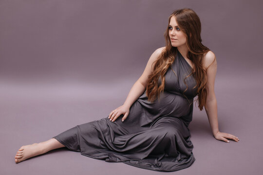 Pregnant woman in long dress sitting in studio
