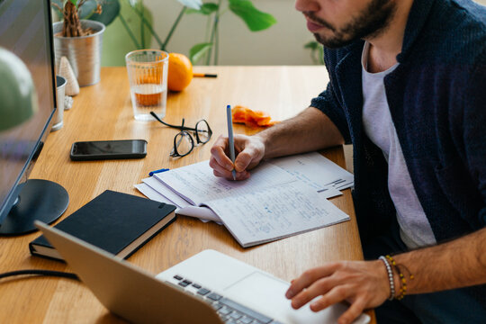 Unrecognizable young adult man writing in notebook 