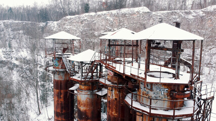 Fototapeta na wymiar Liban quarry Kamieniolom in Krakow, Poland during the winter season. Old rusty machinery and piping equipment in closed limestone. Jurassic limestone cliffs and old, rusty industrial buildings. 