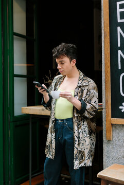 Young extravagant gay man outside a city cafeteria checking his phone