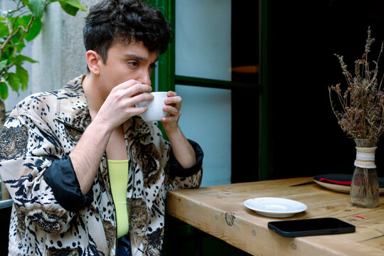Young extravagant gay man drinking hot beverage