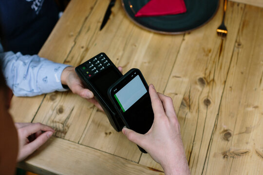 Detail shot from above of hand holding a smart phone doing a wireless payment at a restaurant