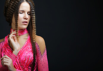 Young woman with creative hairstyle wearing pink dress over black background.