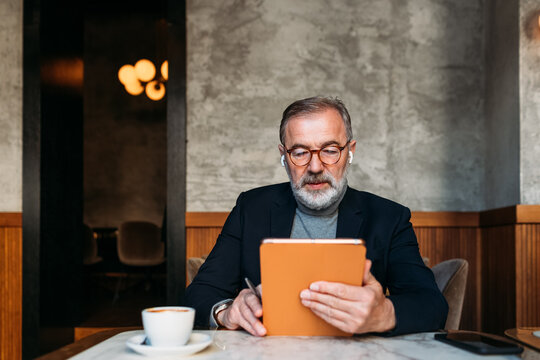 Senior Man Using Digital Tablet in Cafe - Powered by Adobe