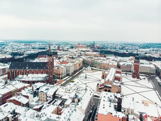 Rolgordijnen Panoramisch uitzicht op het centrale plein in Krakau, Polen, omringd door historische herenhuizen (kamienice) en kerken. Straten bedekt met sneeuw in het winterseizoen. Heldere witte lucht op de achtergrond. © CameraCraft