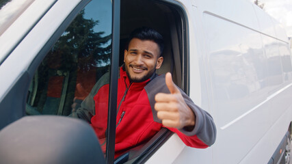 Delivery guy wearing red uniform sitting in the white van making a thumbs up sign. Happy Indian guy...