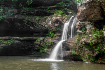 Fototapeta na wymiar Water cascades down tiers of worn sandstone at the Upper Falls, a beautiful waterfall at Old Man’s Cave in Hocking Hills State Park, Ohio seen in profile from the side.