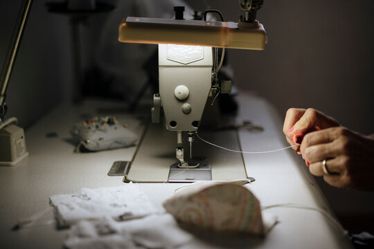 Close-up view of embroidery machine under dim light, hands preparing embroidery thread