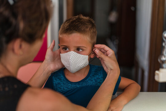 Woman looking face to face with her son while he puts on protective mask