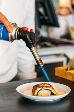 Crop chef preparing sushi and using gas torch
