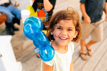 Gleeful child with a balloon animal on her shoulder. 