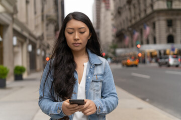 Young Asian woman in city walking texting cellphone on a street