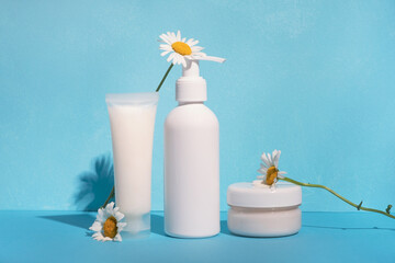 Cosmetic products with chamomile flowers on bright blue wall background. Still life natural organic cosmetics with sunlight shadows. Beauty treatment concept, skincare