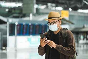 Young traveler man wearing mask to protect flu coronavirus using smartphone to check in Arrival or...