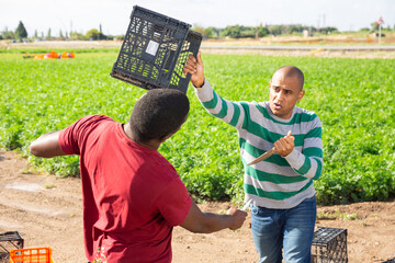 Aggressive hispanic farm worker with knife and plastic box in hands fighting with his african...