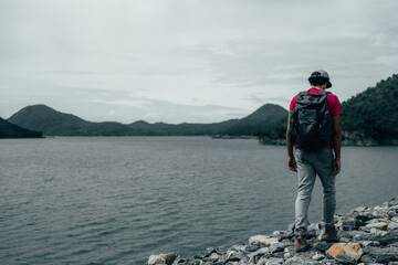 young teen Caucasian boy hipster man adult backpacker enjoying camera on beautiful landscape scenery view jungle mountains forest at Kanchanaburi water river dam National Park, Thailand.