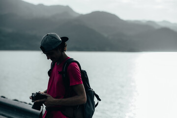 young teen Caucasian boy hipster man adult backpacker enjoying camera on beautiful landscape scenery view jungle mountains forest at Kanchanaburi water river dam National Park, Thailand.