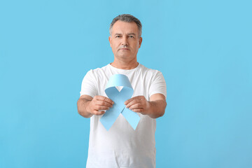Mature man with blue ribbon on color background. Prostate cancer awareness concept