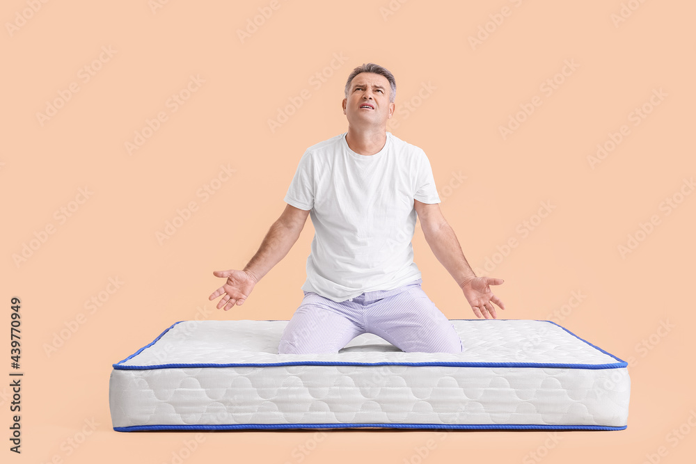 Sticker Troubled mature man sitting on soft mattress against color background