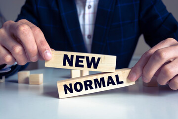 Obraz premium Man use their fingers to touch the word New normal on a wooden block. New lifestyle changes in order to balance, including business, economy, environment and health for Make a big dramatic change.