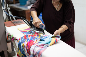 An Asian elderly woman who is a housewife is ironing clothes with an iron, which is a household chore.