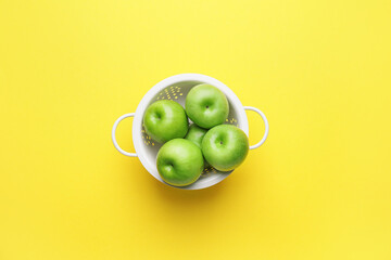 Colander with fresh green apples on color background