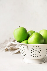 Colander with fresh green apples on table