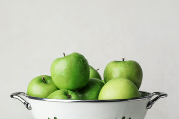 Colander with fresh green apples on light background