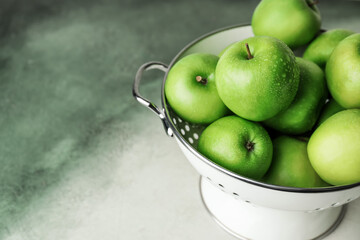 Colander with fresh green apples on color background