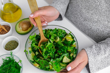 Woman mix salad of fresh green vegetables and herbs. Raw food concept. Vegan menu. Cooking healthy...