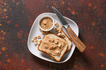 Plate with tasty peanut butter and bread on color background