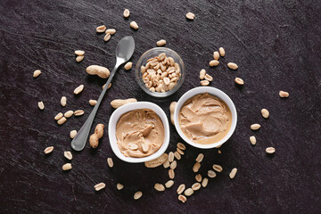 Bowls with tasty peanut butter on dark background